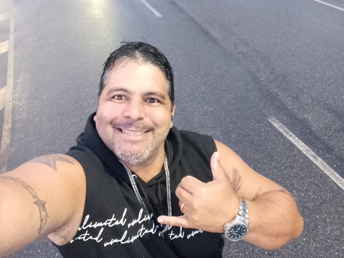 Maurício sorrindo, polegar para cima, na beira da estrada.